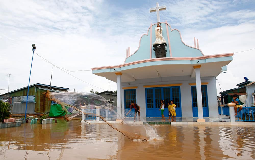 An ethnic Vietnamese boy, left, casts his fishing net onto floodwaters in front of a church along the Mekong river in Koh Phos village, Kandal province, near Phnom Penh, Cambodia.
