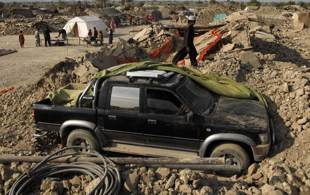 A Pakistani boy walks by a vehicle dug out of the rubble of houses, which were destroyed in Tuesday`s earthquake, in the remote district of Awaran in Baluchistan province, Pakistan.