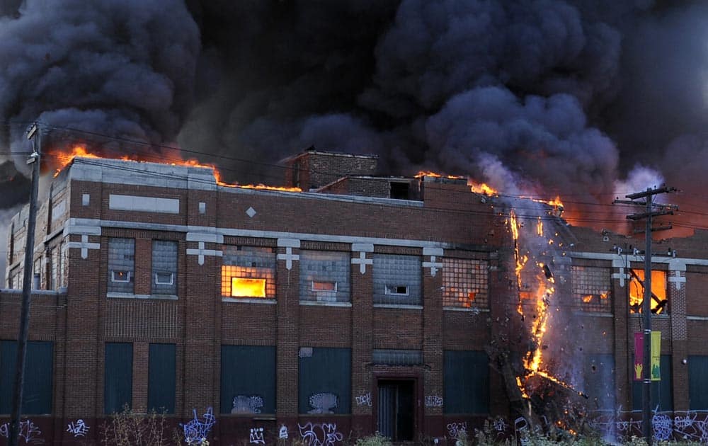 A part of the wall of an abandoned building in Detroit collapses in flames as Detroit firefighters try to contain the fire, in Detroit, Mich.