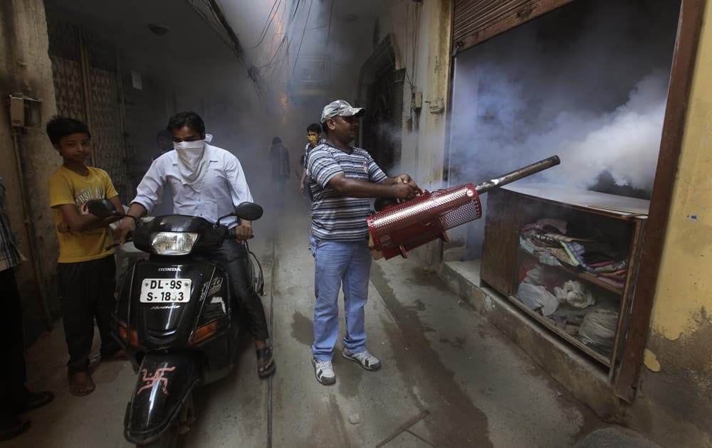A man rides a motorbike past a Delhi municipal worker fumigating the area to prevent mosquitos from breeding in New Delhi.