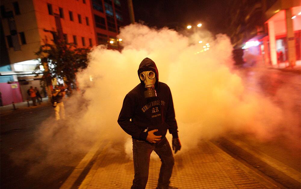 A protester wearing a gas mask leaves after trying to throw back a tear gas canister to riot police during a protest against far-right Golden Dawn party, in Athens.