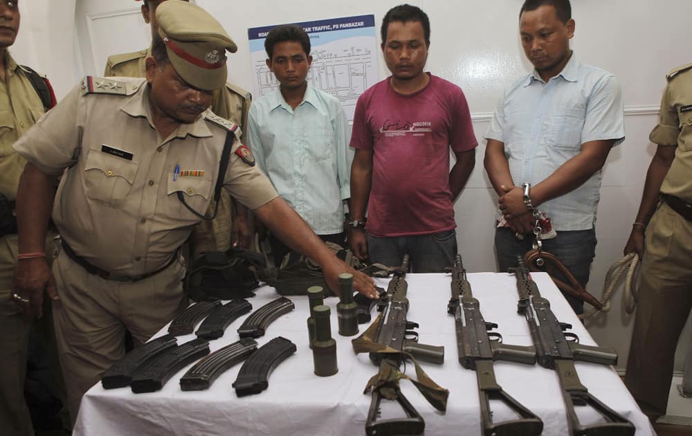 Police display arms and ammunition they claim to have seized from three suspected rebels of the United Liberation Front of Assam (ULFA), three men standing behind, in Guwahati.