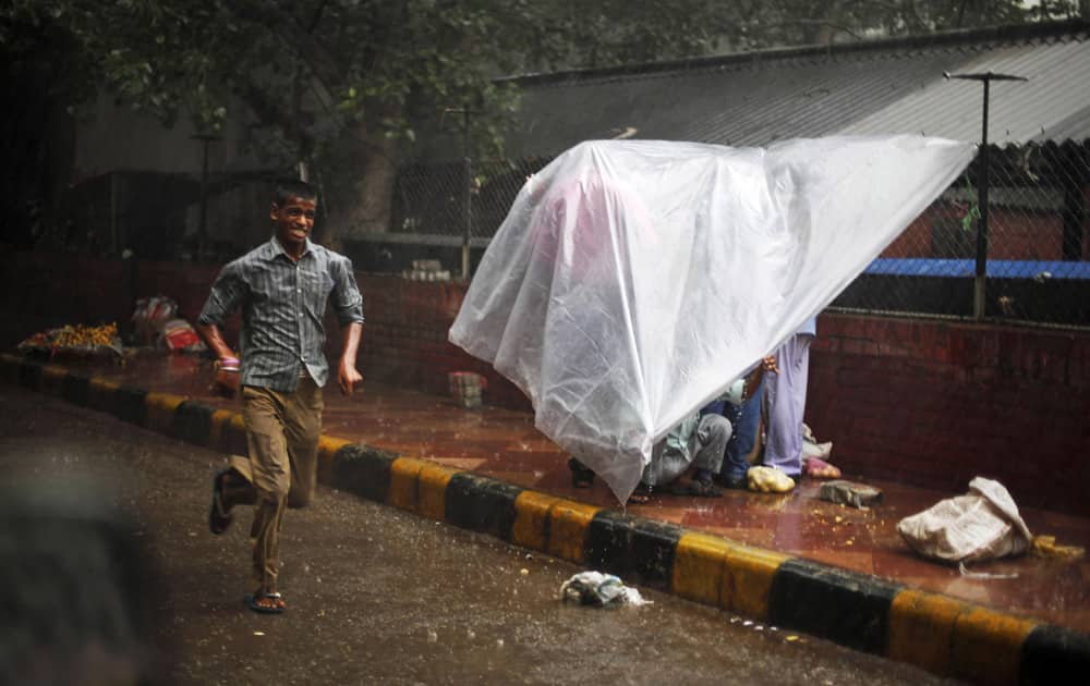A boy runs for shelter as others take refuge under a plastic sheet on a sidewalk during a sudden downpour in New Delhi.