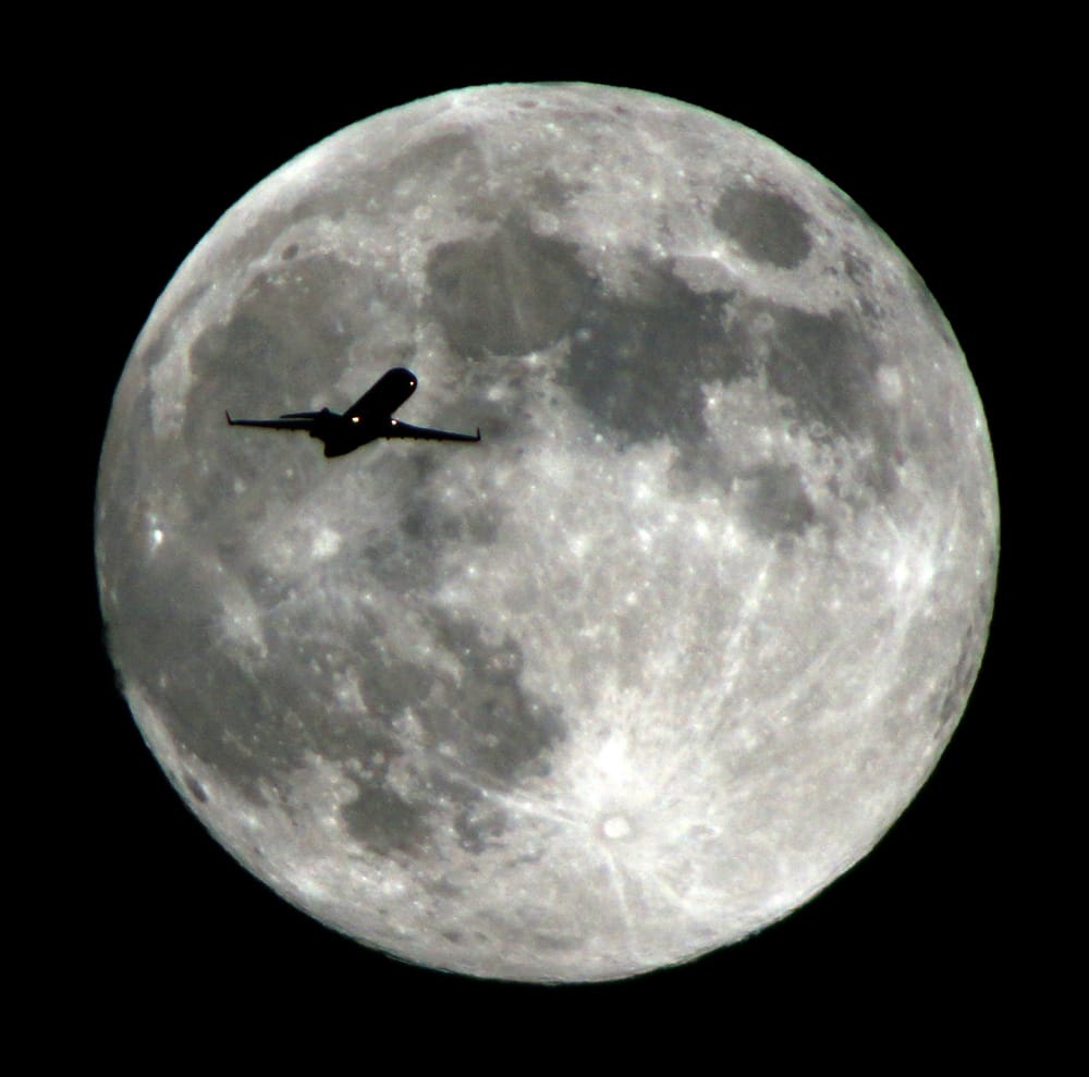 An airlines jet plane approaching Los Angeles International Airport crosses the moon as seen from Monterey Park Calif.