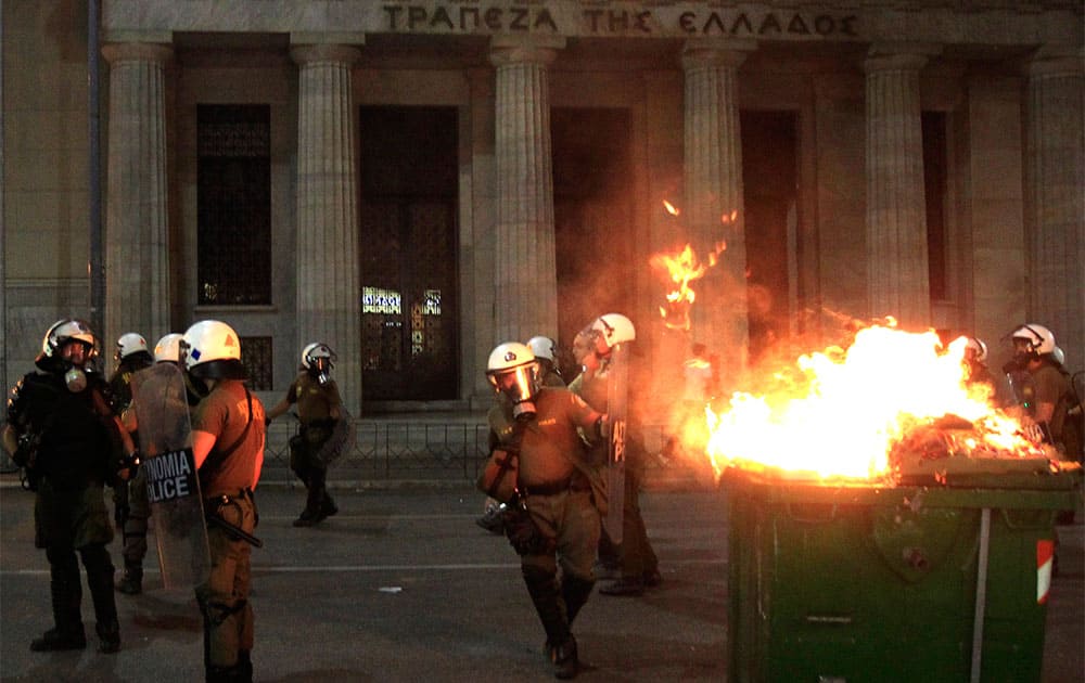Riot police walk past a burning garbage bin in front of the Bank of Greece during a protest in Thessaloniki.
