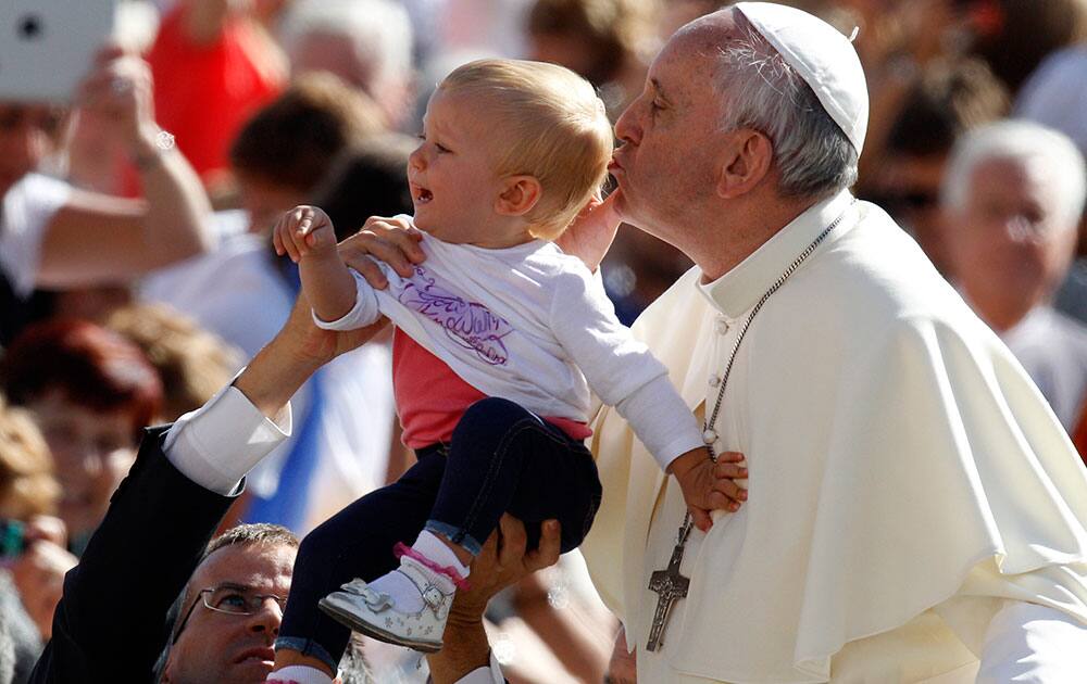 Pope Francis kisses a child as he arrives for his weekly general audience in St. Peter`s Square at the Vatican.
