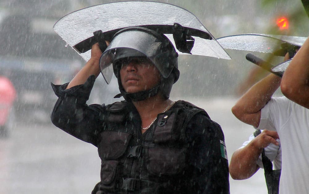 A riot policeman, helping to guard the entrance of a hotel from protesting teachers, uses his shield as protection from heavy rains, in the Caribbean resort city of Cancun, Mexico.