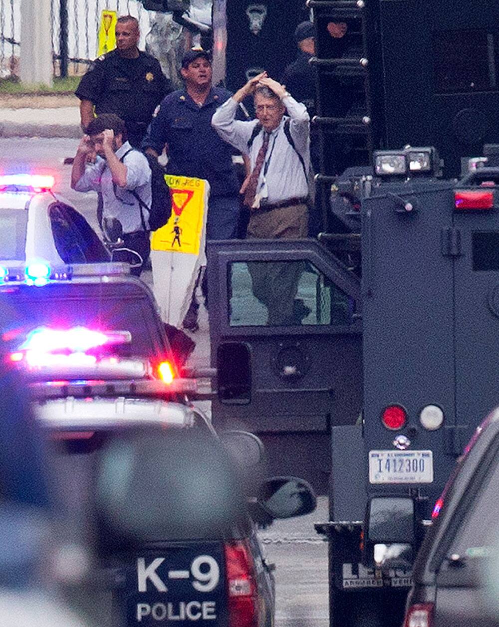 People hold their hands to their heads as they are escorted out of the building where a gunman was reported at the Washington Navy Yard in Washington.