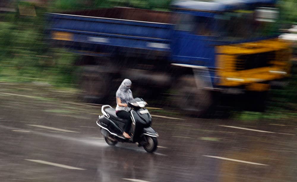 A woman rides a scooter with her face covered with a scarf to protect her from rain in Hyderabad.