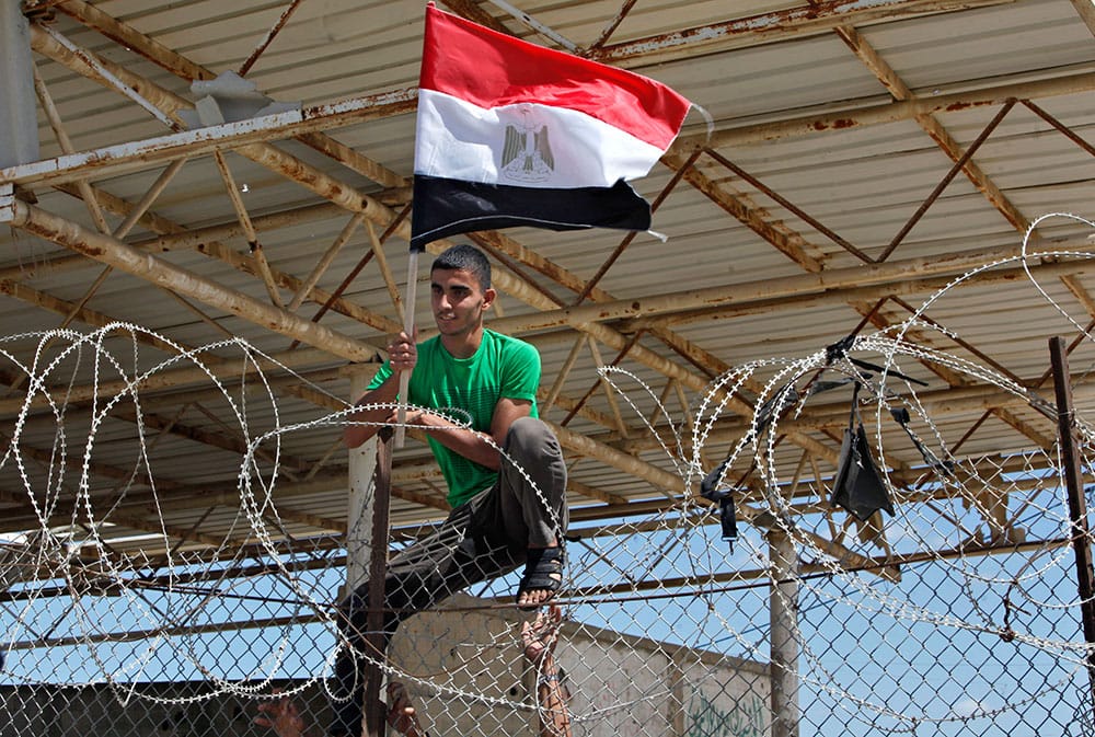 A Palestinian demonstrator climbs a fence with Egyptian flag during a protest calling on Egypt to reopen the Rafah border crossing in Rafah, southern Gaza Strip.