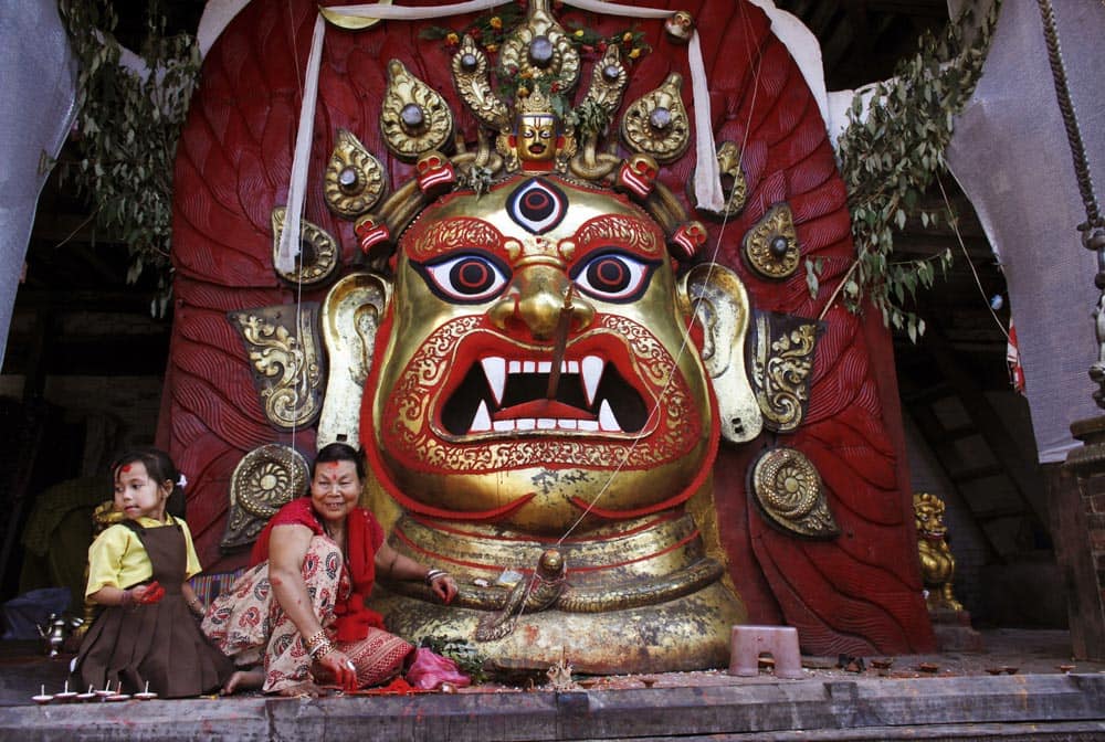 A Nepalese woman and a girl sit in front of a statue of Hindu deity Swet Bhairav during the last day of the week-long Indra Jatra festival in Katmandu, Nepal.