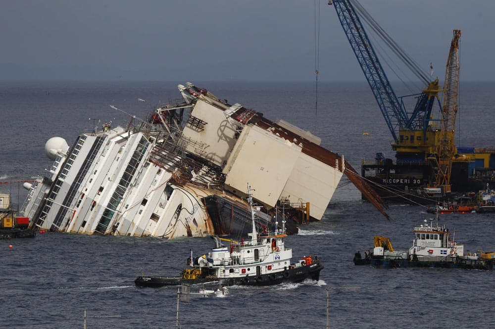 Tow boats sail past the Costa Concordia ship as it lies on its side near the Tuscan Island of Giglio, Italy.