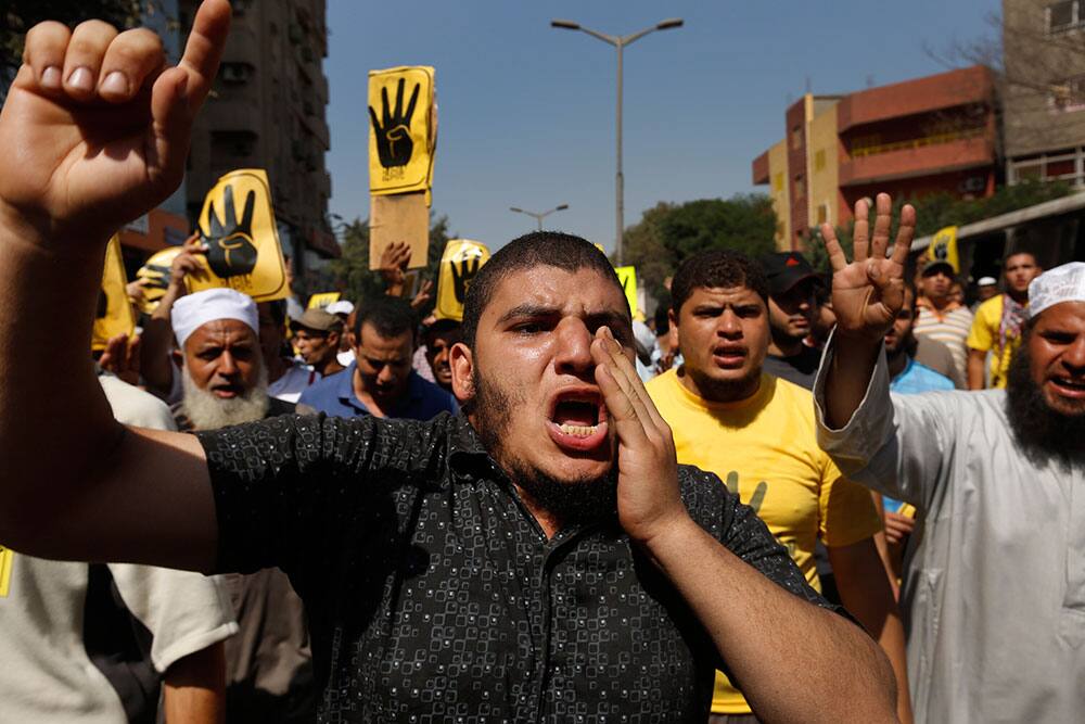 Supporters of Egypt`s ousted President Mohammed Morsi chant slogans as others hold placards with a sign of an open palm with four raised fingers, which has become a symbol of the Rabaah al-Adawiya mosque, where Morsi supporters were violently dispersed in August, during a protest in Cairo, Egypt.