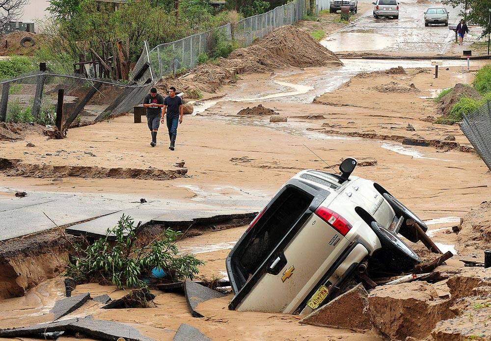 La Union resident George Enriquez, left, and Pablo Romero of Las Cruces, N.M. survey the damage along Sentenario Street in La Union, N.M. where Thursday`s massive flooding destroyed multiple roads in the small town.