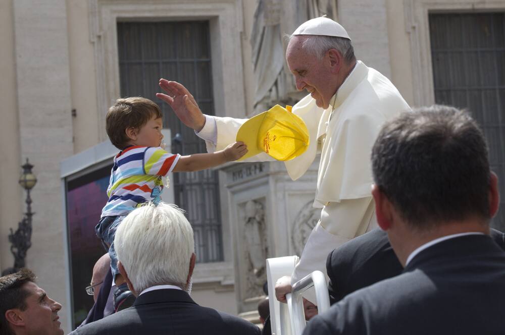 Pope Francis caresses a child who is handing him a hat as he leaves in his car after his weekly general audience in St. Peter`s Square at the Vatican.