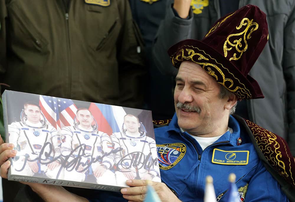 Russian cosmonaut Pavel Vinogradov holds a box of candies with a photo and signatures of Expedition 36 crew members, from left, Chris Cassidy, Vinogradov and Alexander Misurkin during a press conference at the airport in Karaganda, Kazakhstan.