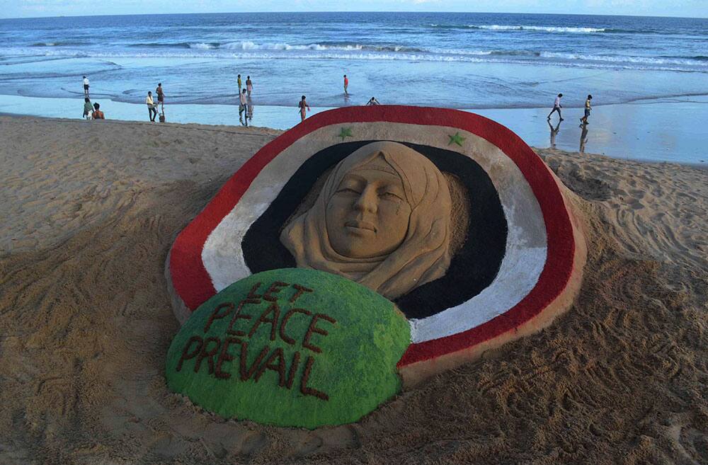 People walk past a sand sculpture on Syria created by Indian sand artist Sudarshan Pattnaik on the Bay of Bengal coast at Puri, Orissa state, India.