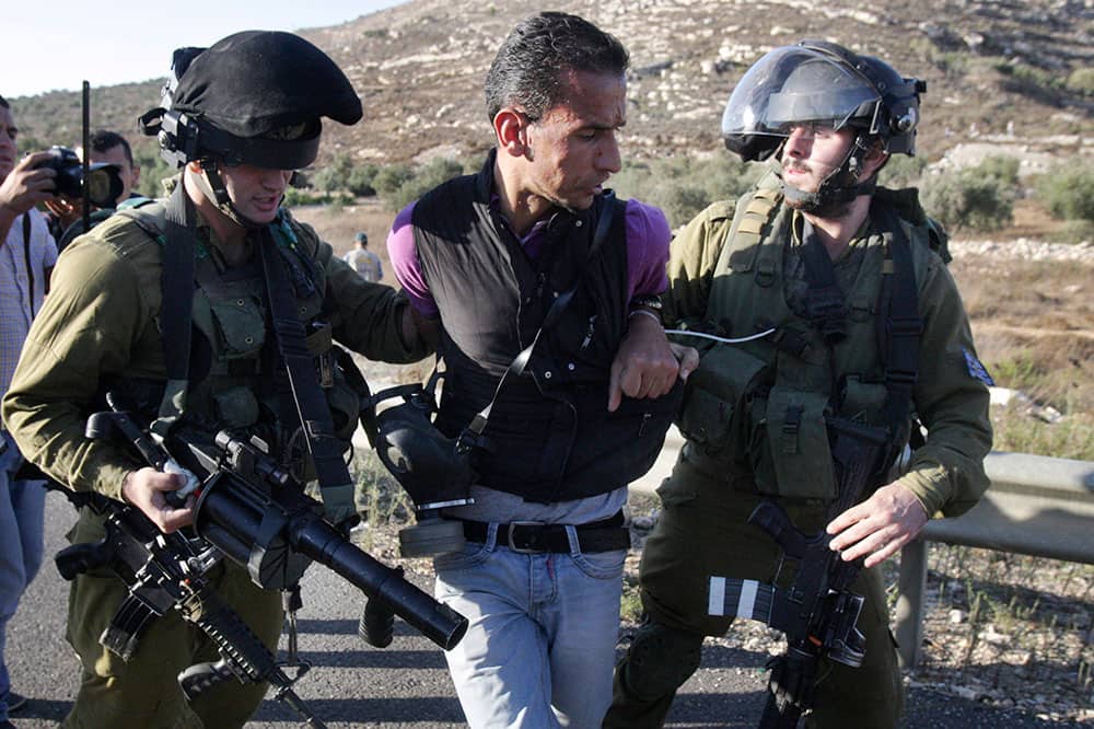 A Palestinian man is detained by Israeli soldiers during a protest near the West Bank village of Qaryout near Nablus. Palestinians protested the closure of a road to their village.