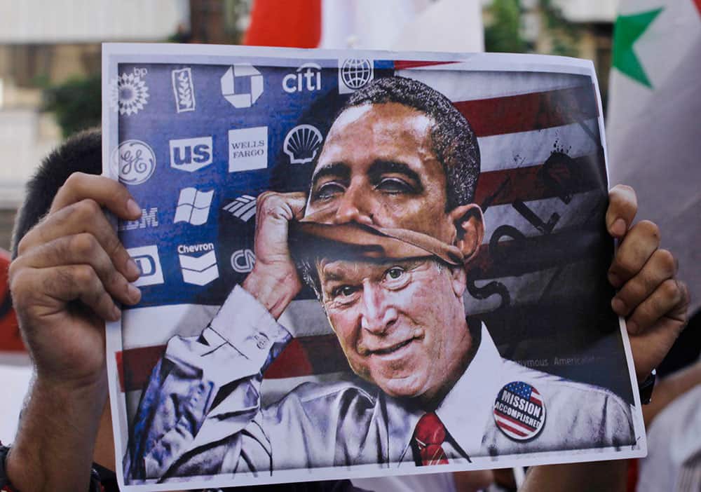 A man holds a poster depicting former US president George W. Bush putting on a mask of US President Barack Obama during a demonstration against a possible military strike in Syria, near the US Embassy in Awkar, east of Beirut, Lebanon.