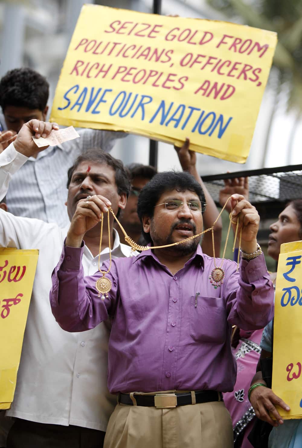 A member of a social organization holds gold ornaments and Indian currency notes and shouts slogans along with others during a protest asking the government to ban import of gold, in Bangalore.