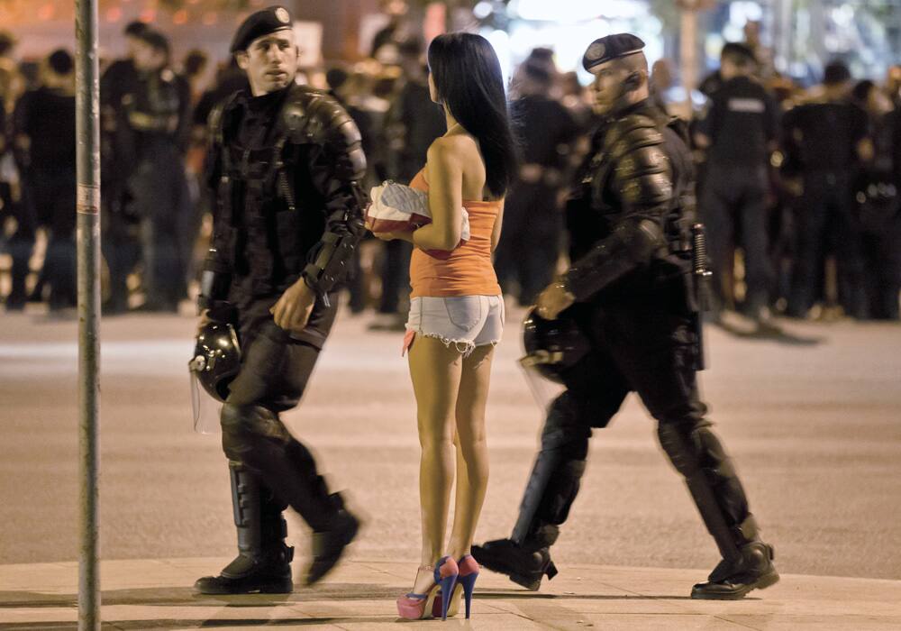 Romanian riot policeman prepare to confront protesters, as a woman views the scene and demonstrators gather nearby, in Bucharest, Romania.