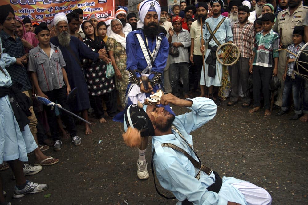 A Sikh man breaks a coconut placing it on the forehead of another as they display martial art skills during a procession to mark the installation anniversary of the Guru Granth Sahib, Sikhism’s holy book in Amritsar.