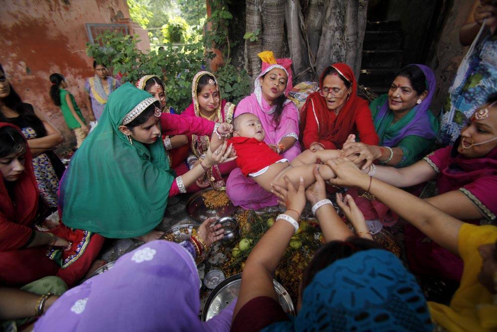 Hindu women belonging to the Dogra community swing a child as part of a ritual as they pray for the long life of their sons during the
