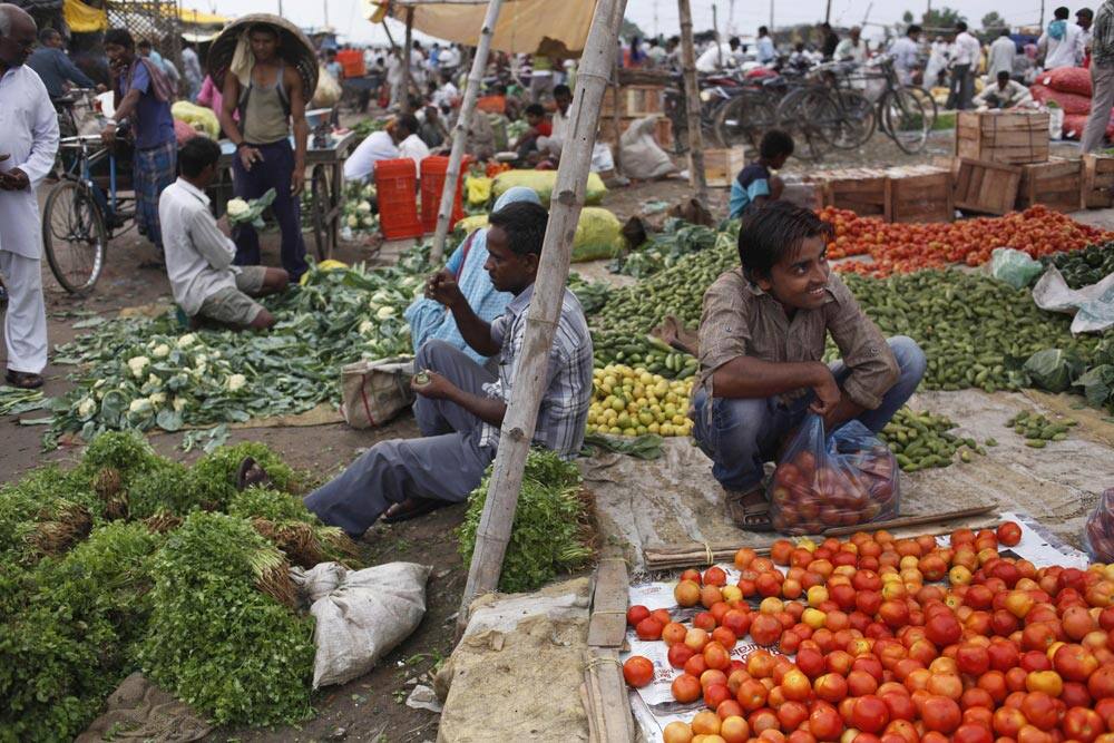 An Indian vendor, right, reacts to a customer as he sells tomatoes at a wholesale vegetable market in Allahabad.