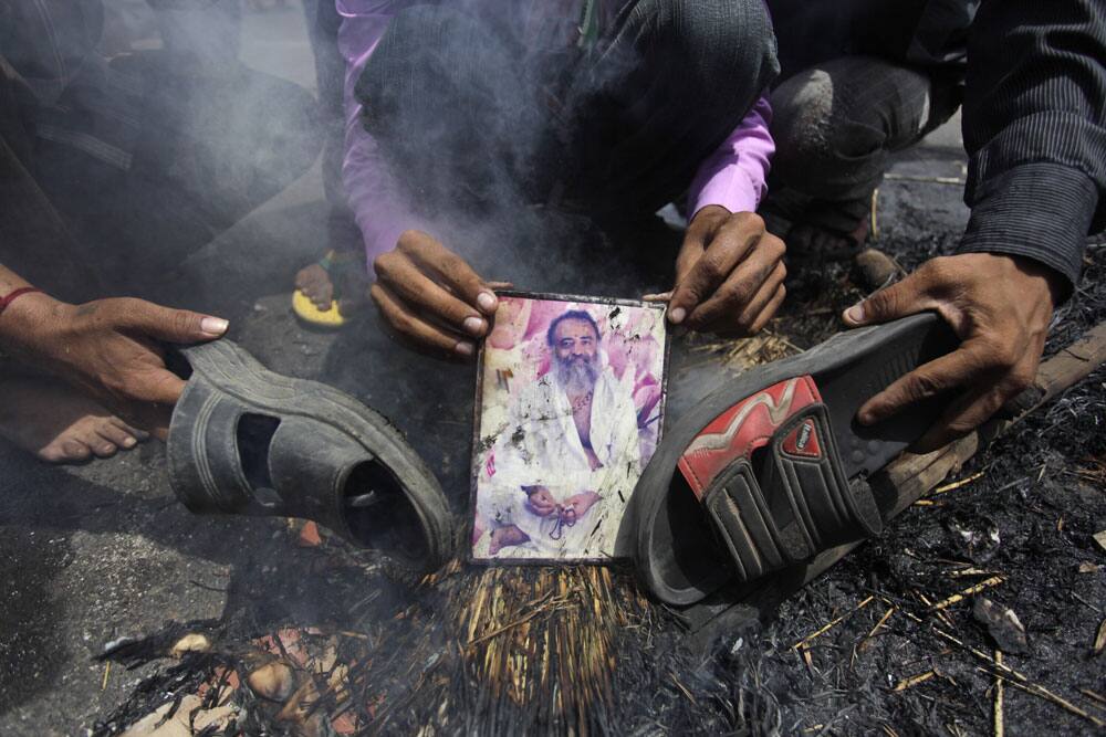 An Indian supporter of India`s ruling Congress party holds a burning photograph of Indian godman Asaram Bapu as others beat it with footwear during a protest in Ahmadabad.