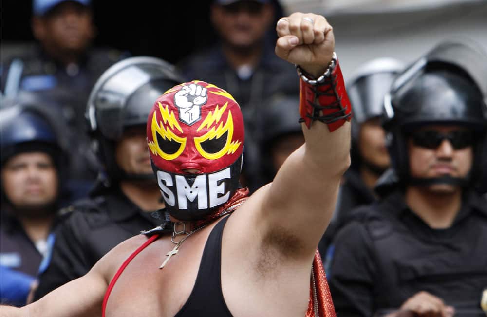 A protester dressed as a wrestler representing the Mexican Electrical Workers Union, SME, raises his fist backdropped by a cordon of riot police, during a march against President Enrique Pena Nieto`s proposed energy reform that would allow private companies to explore the country`s oil and gas reserves, in Mexico City.