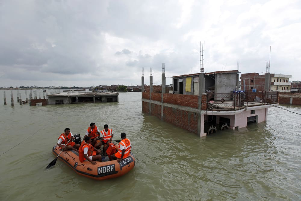 Members of India`s National Disaster Response Force (NDRF) ride an inflatable boat on the flooded banks of the River Ganges after heavy monsoon rains in Allahabad.