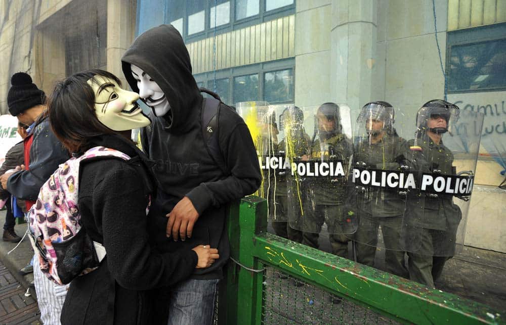 A couple of masked protesters stand near riot police guarding a public building during a rally in Bogota, Colombia.