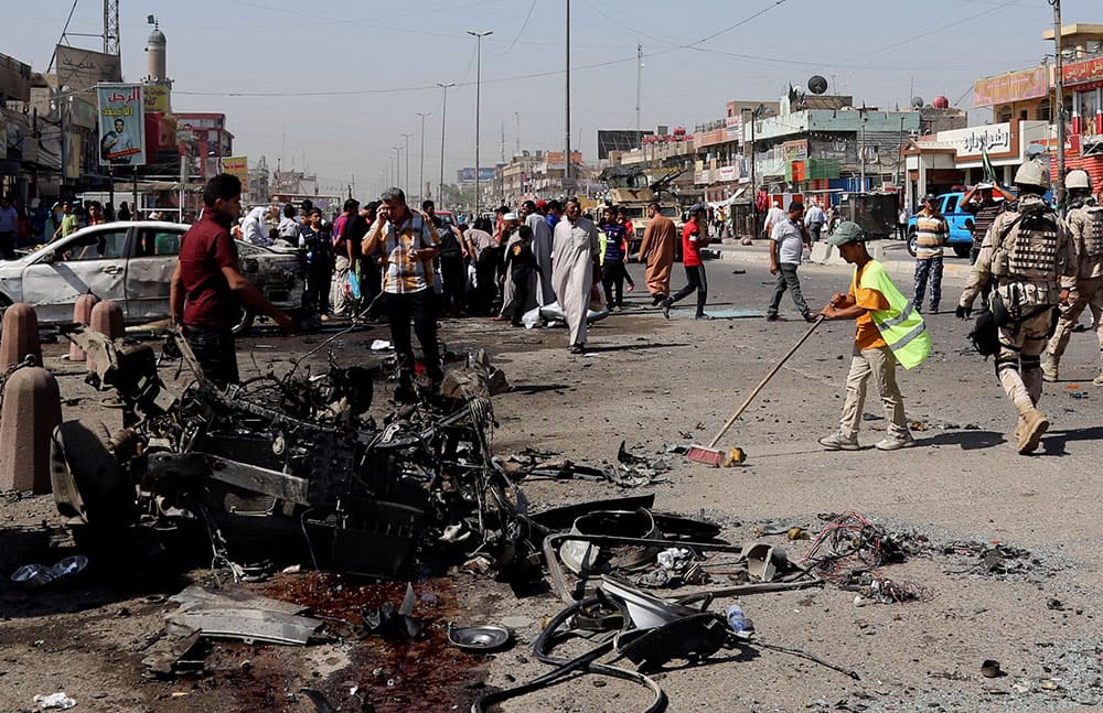 A Baghdad municipality worker cleans, while people and security forces inspect the site of a car bomb attack in Sadr City, Baghdad, Iraq.