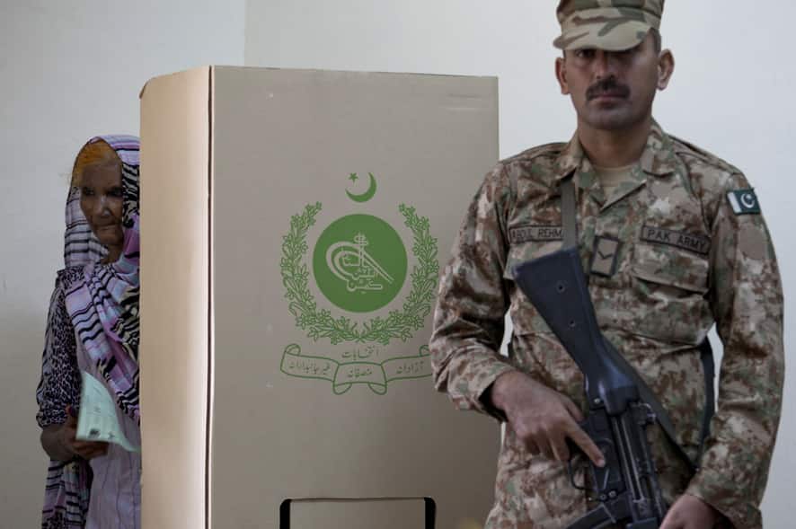 An elderly woman carries a ballot as a Pakistani army soldier stands alert during elections in Islamabad, Pakistan.