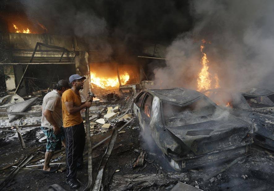 Lebanese citizens stand next to burned cars and shops at the site of a car bomb explosion, in an overwhelmingly Shiite area and stronghold of the Lebanese militant group Hezbollah, at the southern suburb of Beirut, Lebanon.