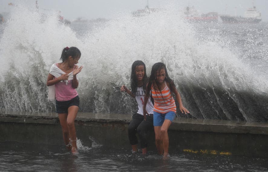 Filipino girls react as a big wave approaches while they play at a flooded park in Navotas, north of Manila, Philippines.