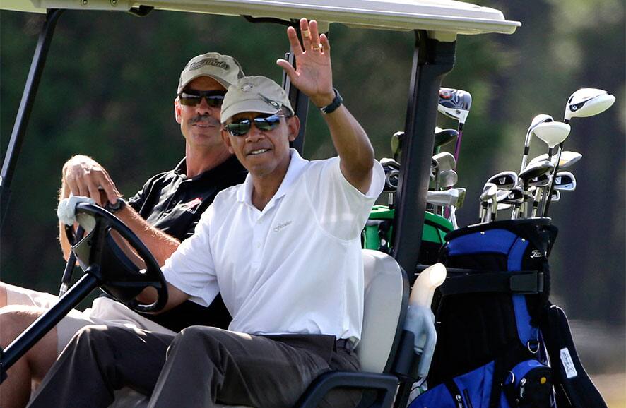 President Barack Obama, right, waves to a crowd of onlookers while driving a golf cart with businessman Glenn Hutchins, behind, as they golf at Farm Neck Golf Club in Oak Bluffs, Mass., on the island of Martha`s Vineyard.