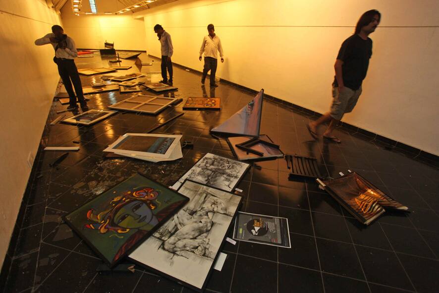 People walks past broken glass and artwork lying on the ground at a gallery displaying a joint exhibit of work by Indian and Pakistani artists in Ahmadabad.