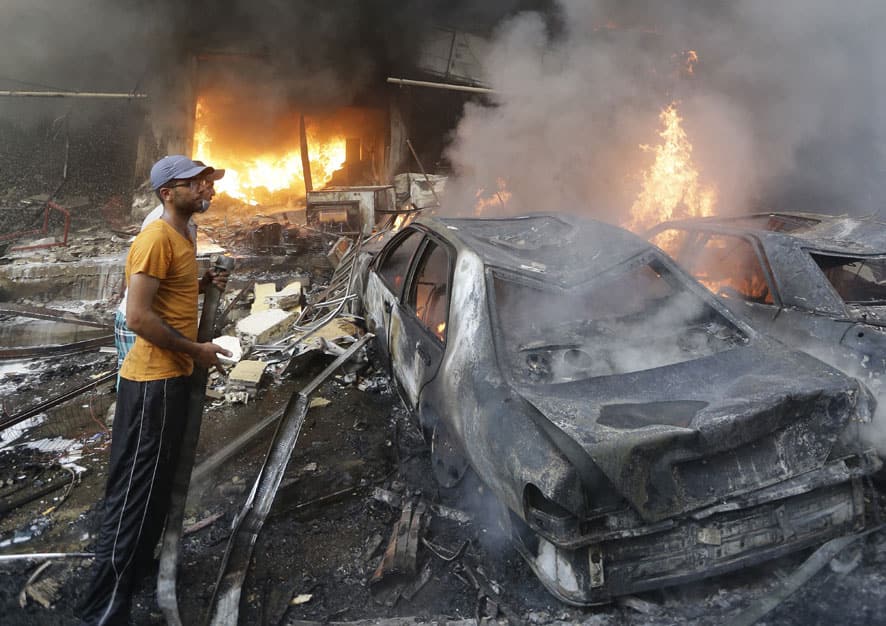 Lebanese citizens stand next to burned cars and shops at the site of a car bomb explosion in southern Beirut, Lebanon.