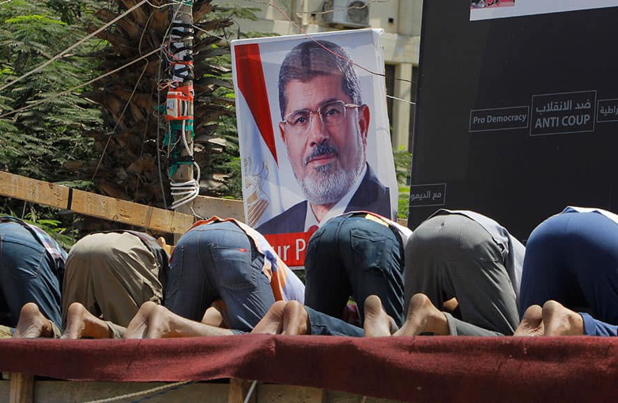 Supporters of Egypt`s ousted President Mohammed Morsi pray in front of his poster in Nahda Square, where protesters have installed their camp near Cairo University in Giza, southwestern Cairo, Egypt.