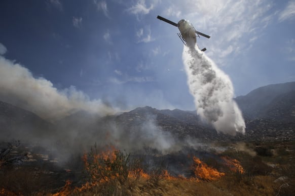 A helicopter drops water over a wildfire in Cabazon, Calif. About 1,500 people have fled and three are injured as a wildfire in the Southern California mountains quickly spreads.