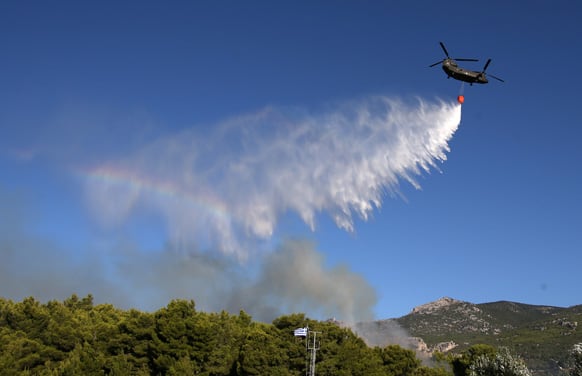 A military helicopter drops water over a burning forrest in Varibobi, a northwestern suburb of Athens.
