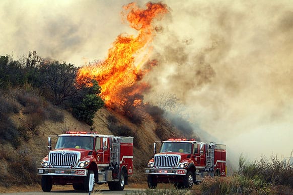 Flames from the Falls Fire burn on a hillside along South Main Divide Road in the Cleveland National Forest as firefighters drive through the area.