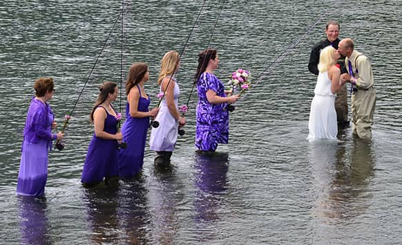 Bridesmaids look on as Kadie and Dake Schmidt, right, exchange a kiss at the end of their wedding ceremony in Kodiak, Alaska`s Buskin River.