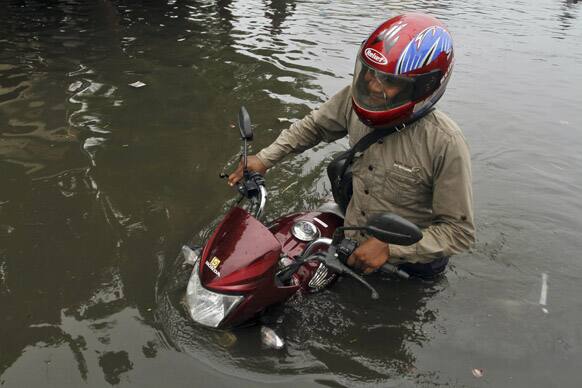 A man pushes his motorcycle as he makes his way through a flooded road after heavy rains in Ahmedabad.