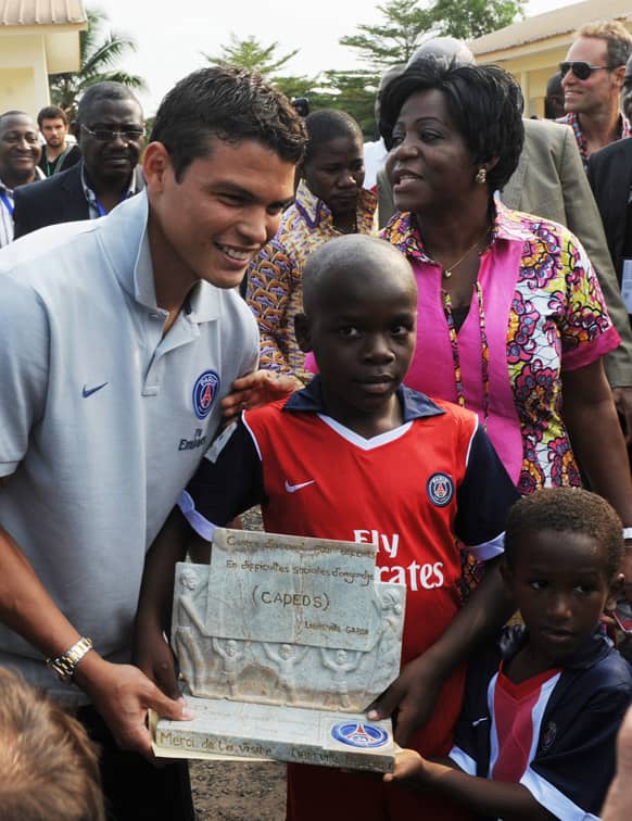 Paris Saint-Germain soccer team captain Thiago Silva, left, receives a gift from children during a team visit to the Angondje Center for Abandoned Children, in Libreville, Gabon.