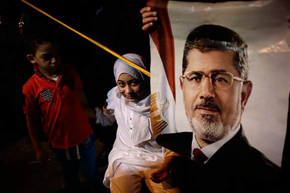 An Egyptian child stands next to poster of the Egypt`s ousted President Mohammed Morsi outside Rabaah al-Adawiya mosque, where supporters have installed a camp and hold daily rallies at Nasr City, in Cairo, Egypt.