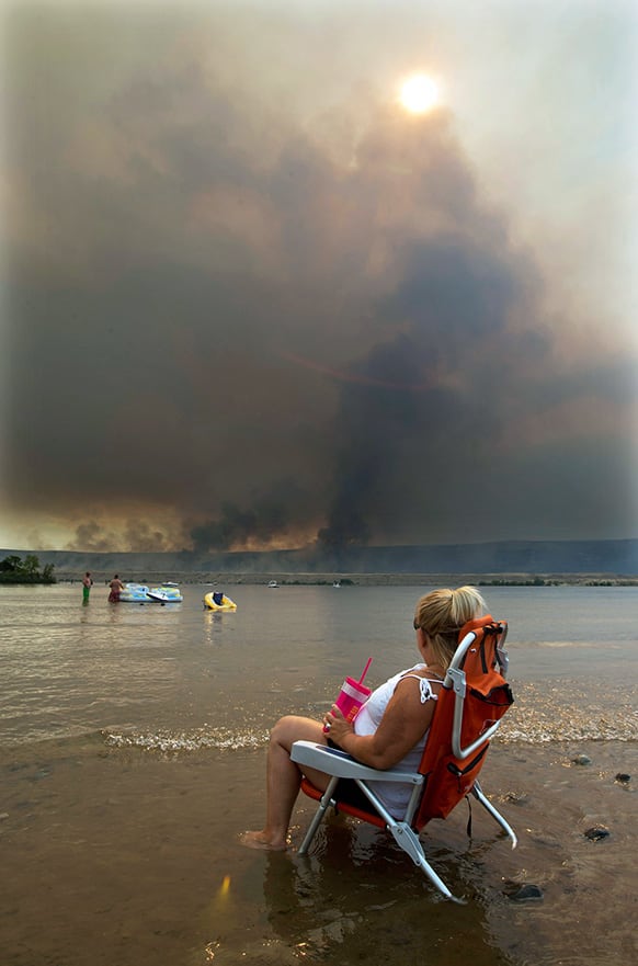 Jody Erickson, of Kent, Wash., watches the Colockum Tarps fire from her beach chair, while sitting on the bank of the Columbia River at the Crescent Bar Resort south of Malaga, Wash.