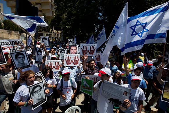 Israeli protesters hold flags, pictures of Israelis who they say were killed by Palestinians, and posters with bloody hands and Hebrew writing that reads,