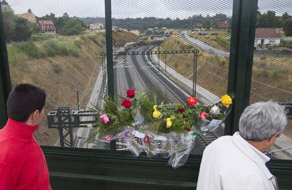 People pass by flowers that were placed on a bridge above the railway tracks at the spot of a train crash in Santiago de Compostela, Spain.
